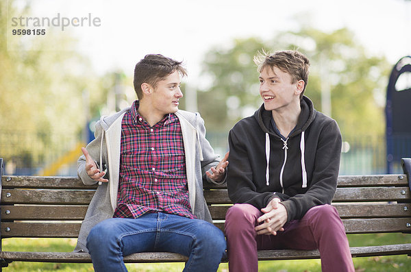 Zwei junge männliche Freunde beim Plaudern auf der Parkbank