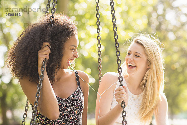 Zwei junge Frauen auf der Parkschaukel sitzend lachend