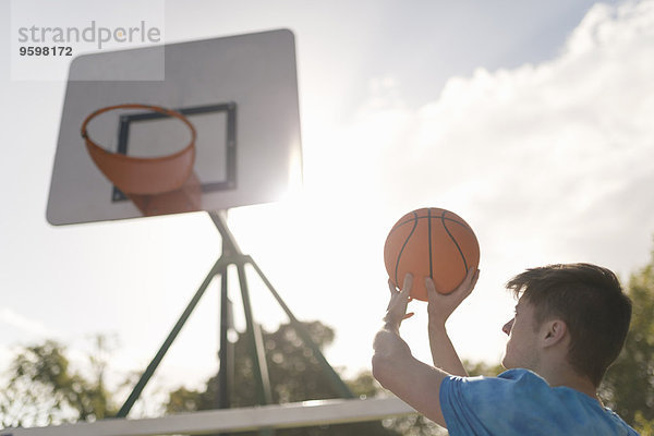 Junger Mann  der Basketball in den Basketballkorb werfen will.