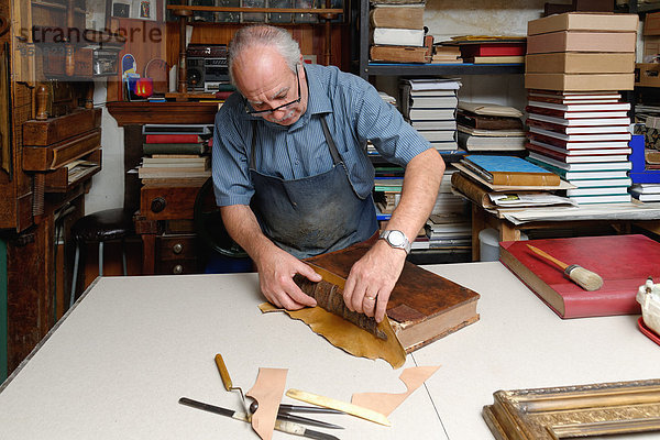 Senior Mann repariert antiken Buchrücken in traditioneller Buchbinderei