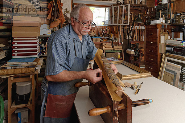 Senior Mann repariert zerbrechlichen antiken Buchrücken in traditioneller Buchbinderei