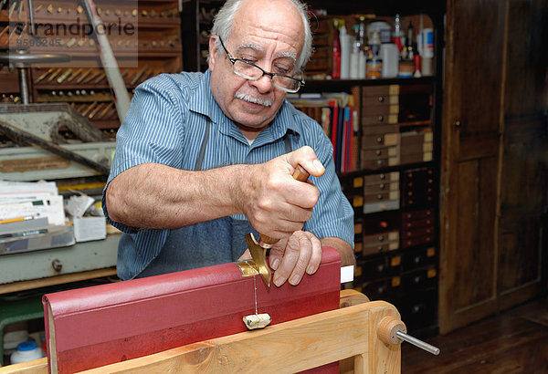 Senior Mann beim Auftragen von Blattgold auf den Buchrücken in der traditionellen Buchbinderei