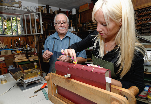Senior-Mann  der in der traditionellen Buchbinderei den Buchrücken mit Blattgold bestreicht.