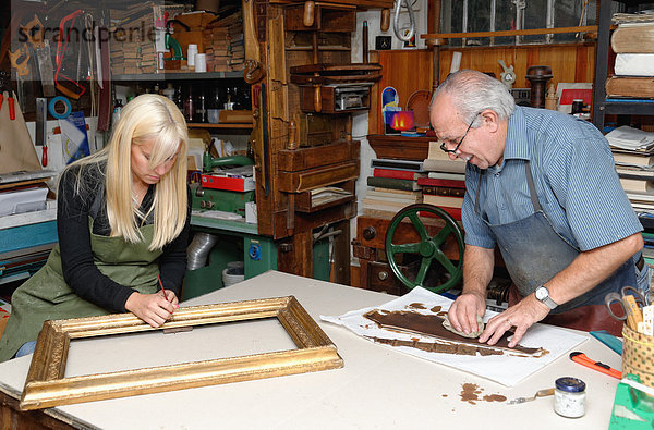 Senior Mann und junge Frau beim Restaurieren von Bilderrahmen und Buchrücken in der traditionellen Buchbinderei