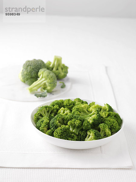 Roher Brokkoli auf Marmor-Schneidebrett und Schale mit gekochtem Brokkoli