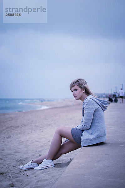 Junge Frau sitzend auf der Seemauer  mit Blick aufs Meer
