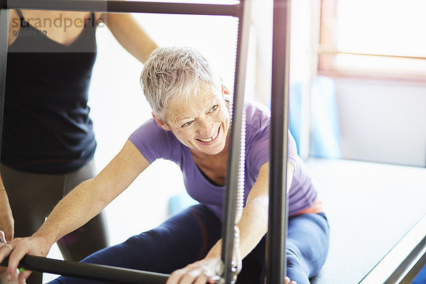 Reife Frau und Tutorin übt Pilates auf dem Trapeztisch im Pilates Fitnessstudio.