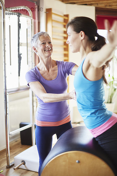 Junge Studentin lehnt sich nach vorne auf Pilates Barrel in der Pilates Turnhalle