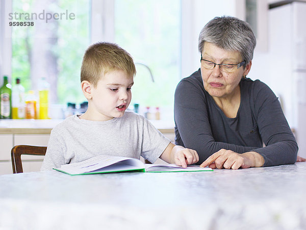 Seniorin liest Märchenbuch mit Enkel am Küchentisch