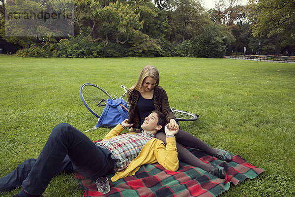 Junges Paar hält Hände auf Picknickdecke im Park