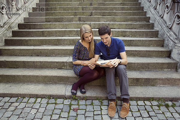 Junges Paar sitzt auf einer alten Treppe und liest Zeitung.