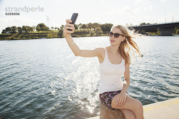 Junge Frau am Flussufer mit Smartphone Selfie  Donauinsel  Wien  Österreich