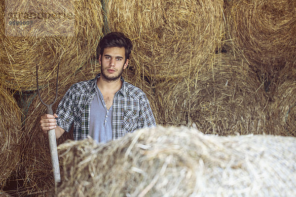 Porträt eines jungen Bauern im Strohstall mit Heugabel  Premosello  Verbania  Piemonte  Italien