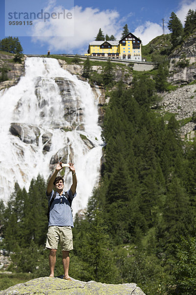 Junger Mann nimmt Smartphone Selfie vor Toce Wasserfall  Formazza  Verbania  Piemonte  Italien