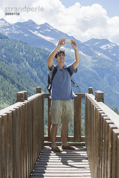 Junger Mann nimmt Smartphone Selfie vor den Bergen  Formazza  Verbania  Piemonte  Italien
