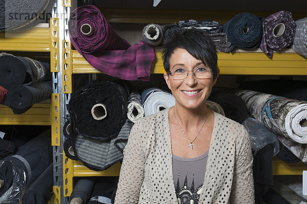 Porträt einer reifen Näherin vor Textilrollen in der Werkstatt