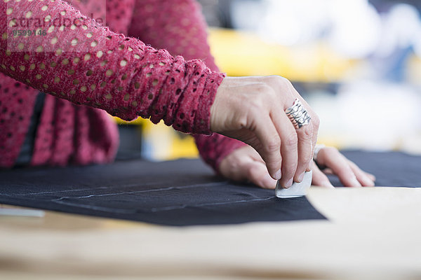 Hände von reifer Näherin Kreidekontur auf Textil auf Arbeitstisch