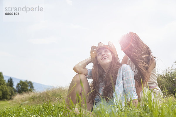 Zwei junge Frauen sitzen im Grasfeld und plaudern.