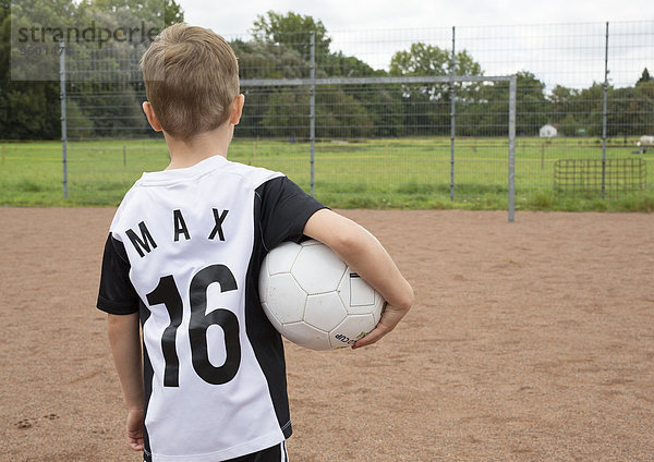 Kleiner Junge auf Sportplatz  von hinten mit Ball unter dem Arm