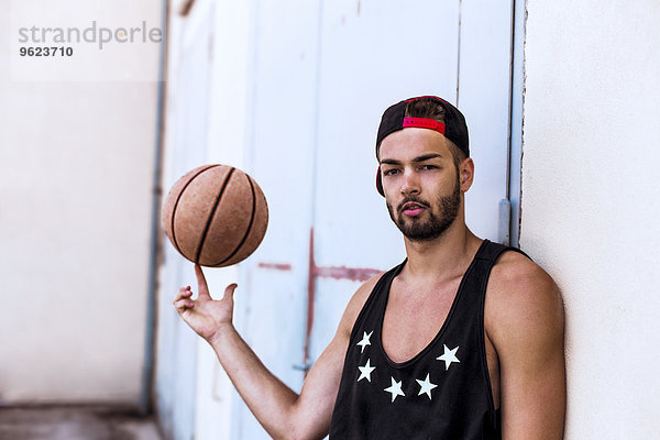 Porträt eines jungen Mannes  der Basketball mit Basecap trägt