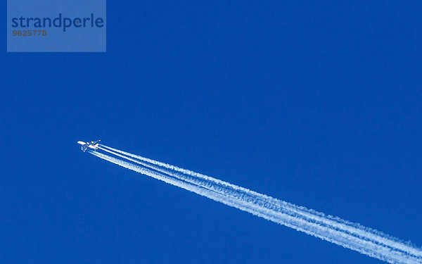 Fliegendes Flugzeug und Kondensstreifen vor blauem Himmel