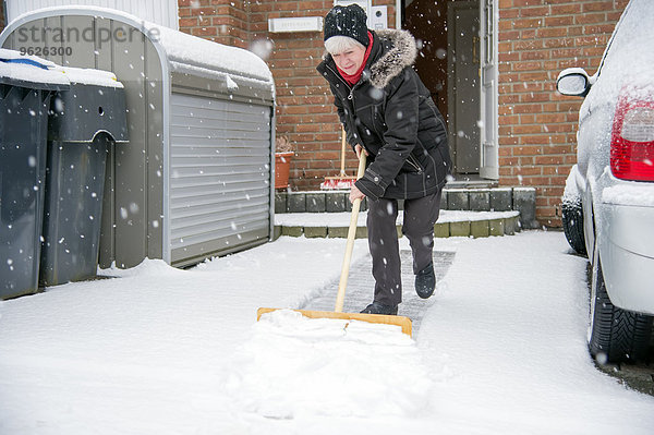 Deutschland  Grevenbroich  Frau beim Schneeschaufeln vor dem Haus