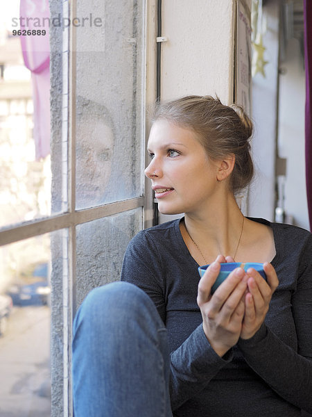 Junge Frau mit Teebogen durchs Fenster schauend