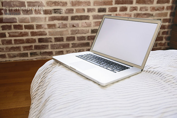 Laptop auf dem Bett stehend vor der Ziegelwand