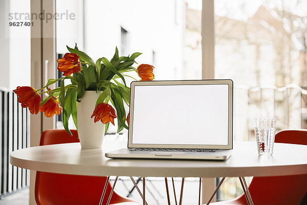 Laptop-Bildschirm auf einem weißen runden Tisch mit roten Tulpen und Stühlen