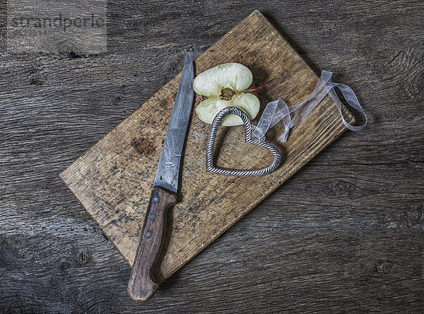 Rustikale Komposition aus geschnittenem Apfel  Schneidebrett  Metallherz und Messer
