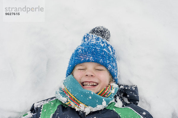 Deutschland  Bayern  Berchtesgadener Land  glücklicher Junge im Schnee liegend