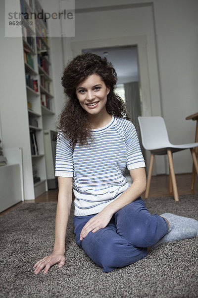 Lächelnde junge Frau zu Hause auf Teppich sitzend
