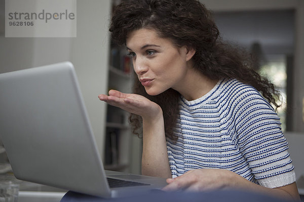 Junge Frau zu Hause am Laptop beim Küssen