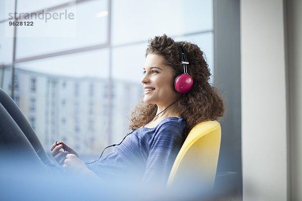 Lächelnde junge Frau mit Kopfhörer am Fenster