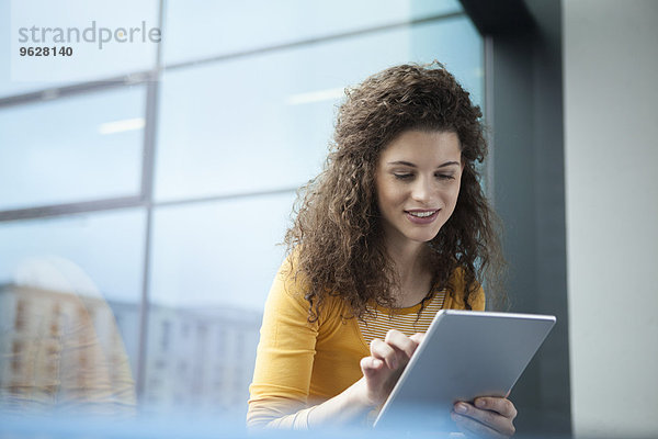 Lächelnde junge Frau mit digitalem Tablett am Fenster