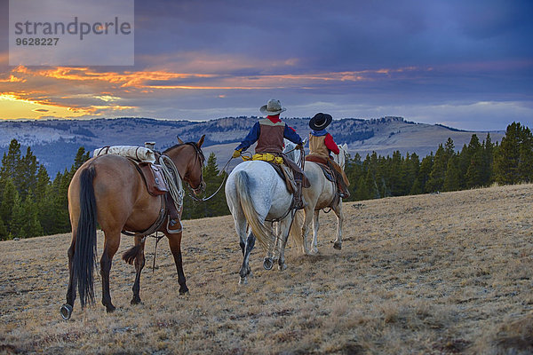 USA  Wyoming  zwei junge Cowboys  die bei Sonnenuntergang in der Wildnis reiten.