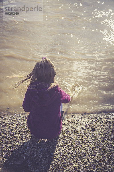 Kleines Mädchen kauert am Wasserrand