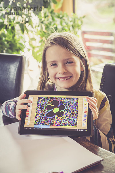 Porträt eines lächelnden Mädchens  das eine digitale Tafel mit ihrer Zeichnung zeigt.