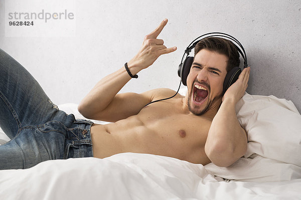 Shirtloser Mann liegt auf dem Bett und hört Musik mit Kopfhörern.