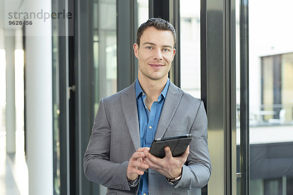 Porträt eines lächelnden Geschäftsmannes mit Tablet-Computer im Büro