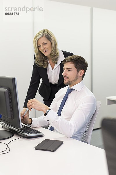 Geschäftsfrau und Geschäftsmann am Schreibtisch mit Blick auf Computerbildschirm