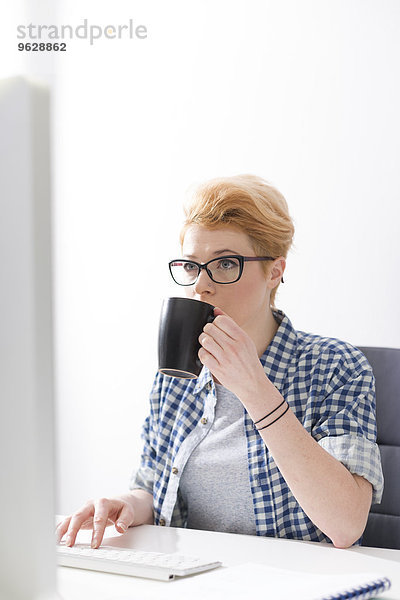 Junge Frau trinkt Kaffee am Schreibtisch