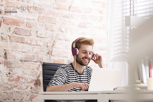 Lächelnder junger Mann mit Kopfhörer am Schreibtisch