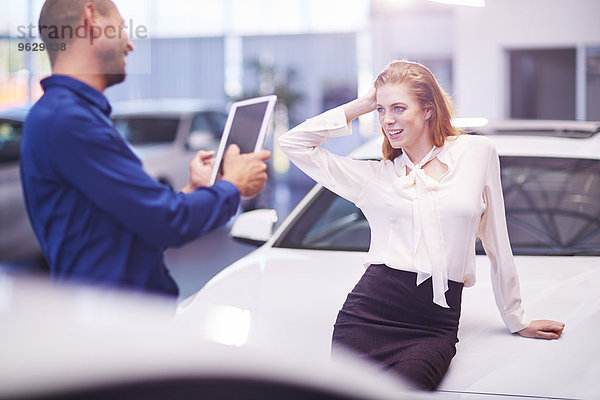 Frau beim Autohändler posiert auf der Motorhaube für ein Foto