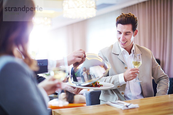 Geschäftsmann sieht Kellner beim Anheben der Servierkuppel im Hotelrestaurant