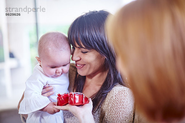 Mutter hält ihr Baby mit einer Frau  die Babyschuhe präsentiert.