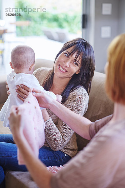 Mutter hält ihr Baby mit Frau hält Babykleidung