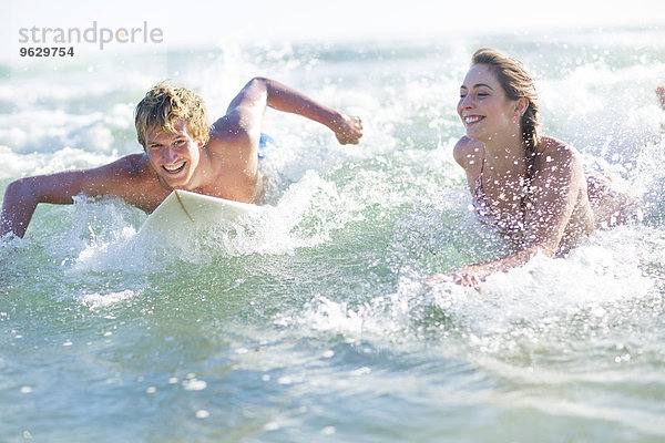 Glückliches junges Paar auf Surfbrettern im Meer liegend