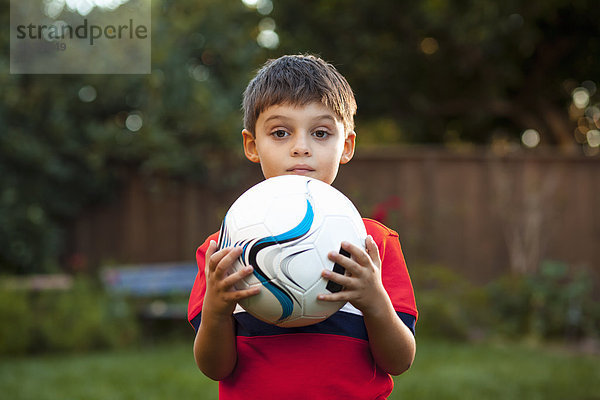 Junge hält Fußball gegen Brust im Garten