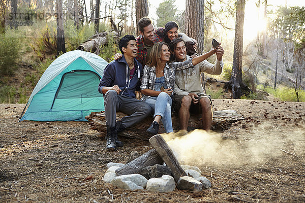 Vier junge erwachsene Freunde nehmen Smartphone Selfie am Lagerfeuer im Wald  Los Angeles  Kalifornien  USA